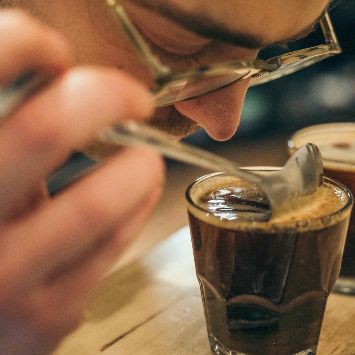 一个男人把鼻子放在一杯咖啡上，以确定它的香气。