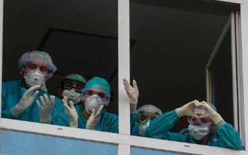 医务人员戴着口罩，戴着手术服，从窗口挥手，传递心语