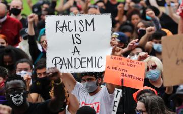 人群中的抗议者举着写着种族主义是流行病的牌子