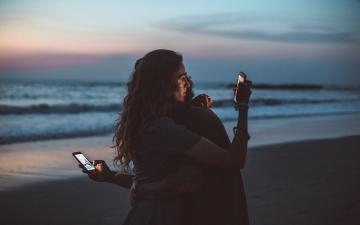沙滩上拥抱的情侣，每个人都看着移动设备的屏幕