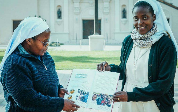 两名ACWECA姐妹在宣教教堂前拿着一本小册子，图片链接到故事