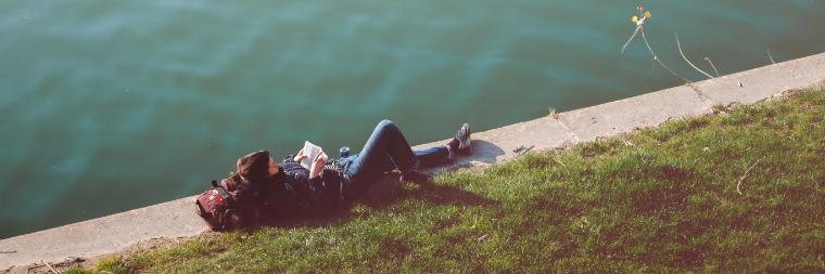 年轻的成年女子躺在水边看书