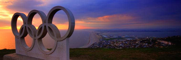 日落时分，一座海滨城市山上的奥运五环雕像